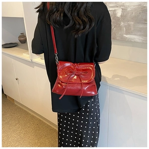 Detail of red glossy shoulder bag with bow knot on black top model background