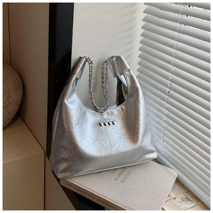 Detail of silver metallic hobo bag with heart studs and chain strap on book