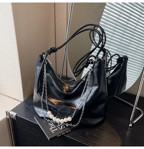Dettaglio borsa hobo nera lucida con grandi perle e ciondoli decorativi a catena