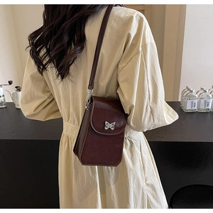 Detail of burgundy crossbody phone bag with silver butterfly clasp in a cafe setting