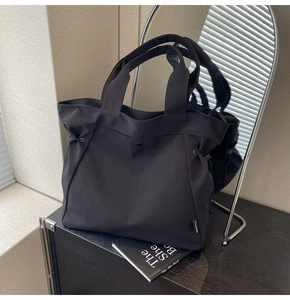 Detail of black canvas tote bag showing side drawstrings and snap button on wooden table