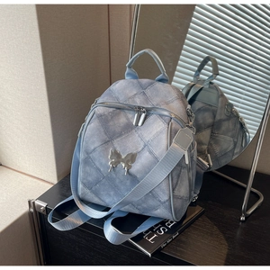 Detail of light blue quilted backpack featuring a metallic butterfly and denim texture