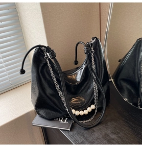 Dettaglio borsa in pelle nera a pieghe con catena d'argento e charm di perle