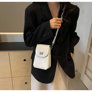 Close-up of white glossy crossbody phone bag with silver butterfly buckle on model