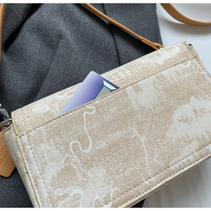 Detail shot of the back pocket on a beige printed crossbody bag with cards inserted