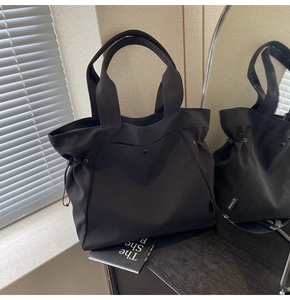 Detail of black canvas tote bag featuring side drawstrings and premium metal button closure