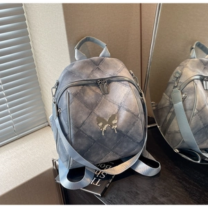 Detail of grey-blue quilted backpack with a silver metal butterfly ornament on a black desk