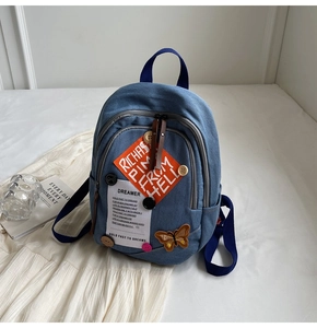 Detail of blue denim backpack with artistic patches, butterfly embroidery and buttons