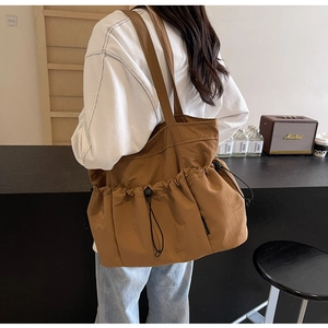 Detail of a large brown tote bag with drawstring pockets on a model in a cafe setting