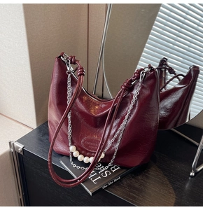 Dettaglio borsa hobo in pelle rosso scuro con catena di perle e trama vintage rifinita