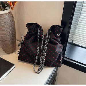 Detail of black drawstring tote bag with red heart patterns and silver chain strap