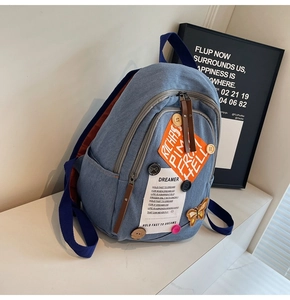 Detail of blue denim backpack showing orange patches, butterfly embroidery and buttons