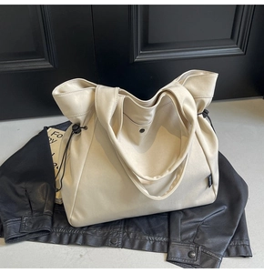 Detail of off-white canvas tote bag with drawstring feature and metal snap closure