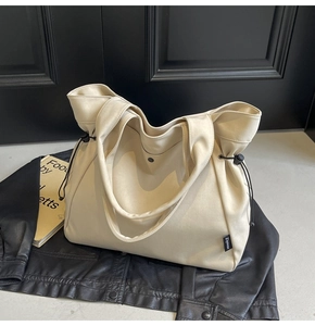 Detailed close-up of a beige canvas drawstring tote bag with dual straps on a black surface