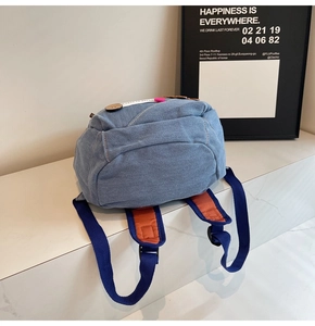 Detail of blue denim backpack with orange padded straps and decorative wooden buttons