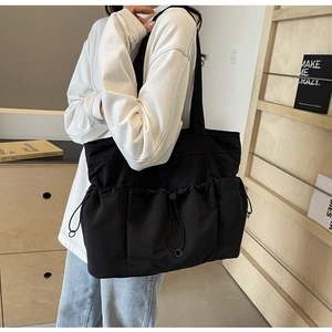 Detail of large black nylon tote bag featuring functional drawstring cargo pockets