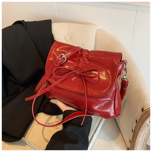 Detail view of a glossy red pleated bucket bag featuring a decorative bow and soft leather