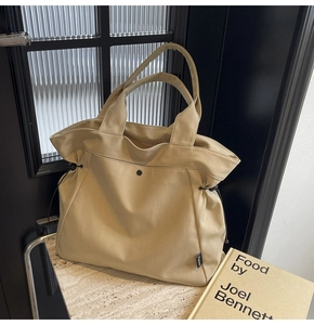 Close-up of beige canvas tote bag with black drawstring details and brand label