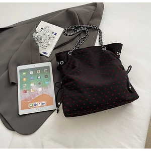 Close-up of black tote bag featuring red heart patterns and silver chain shoulder strap