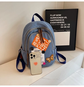 Detail of blue denim backpack with colorful patches and orange labels for school