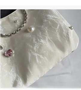 Détail du sac cabas crème avec perles, cristal de cœur rose et bandoulière en chaîne