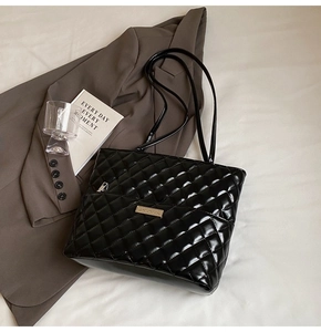 Detail of black glossy quilted tote bag with diamond pattern and gold metal logo plaque