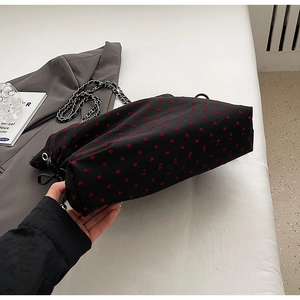 Close-up of black tote bag featuring red velvet heart patterns and silver chain strap