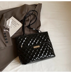 Detail of black quilted tote bag with glossy finish and gold logo on white fabric