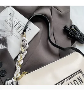 Detail of cream crossbody bag with silk scarf accessory on a grey blazer background