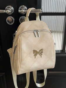 Quilted cream backpack with silver butterfly detail hanging on a dark door handle