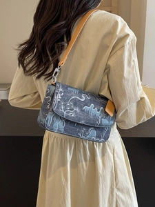 Denim rectangular shoulder bag with white landscape pattern worn by a model in a beige dress