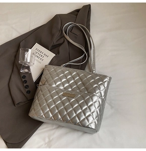 Detail of silver metallic quilted tote bag with logo plate on high-quality fabric