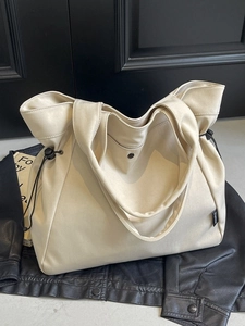 Large beige canvas tote bag with black drawstring details on a stylish black leather jacket