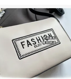 Macro detail of cream leather shoulder bag featuring black Fashion Enjoy embroidery