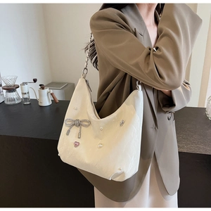 Gros plan d'un sac cabas crème avec nœud en strass, perles et breloques en cœur