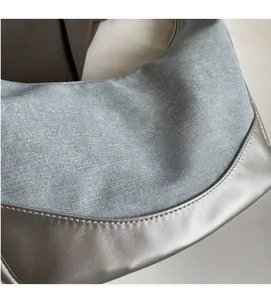 Detail of light blue denim fabric and silver metallic leather stitching on crescent bag