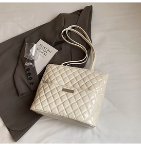 Close-up of quilted cream tote bag featuring glossy patent leather and golden brand nameplate
