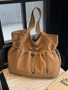 Large tan canvas tote bag with three drawstring front pockets on a stone table