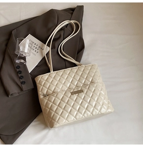 Detail of quilted tote bag with glossy finish, metal logo, and adjustable shoulder strap