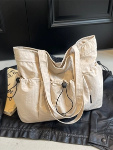Large beige nylon tote bag with pleated design and drawstring pockets on black leather
