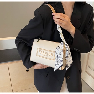 Detail of cream cylindrical crossbody bag featuring a floral silk scarf on the strap