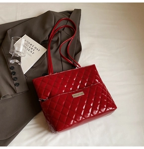 Detailed close-up of glossy red quilted tote bag with metallic logo on a white surface