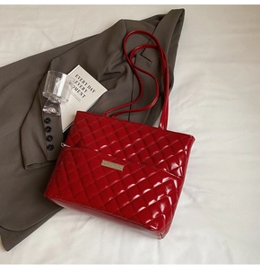 Close-up of a red quilted tote bag with a golden logo plate and glossy finish