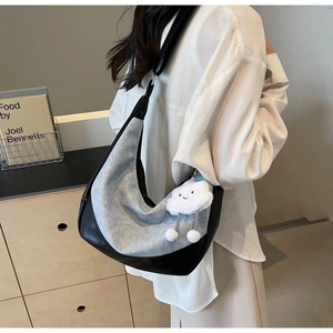 Detail of blue denim and black leather crescent bag featuring a white cloud plush charm