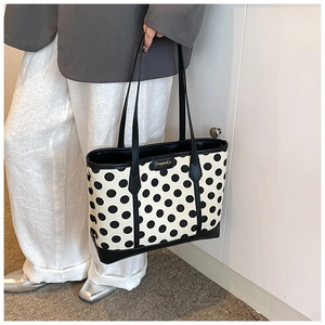 Detail view of polka dot canvas tote bag with leather straps and metal logo plate