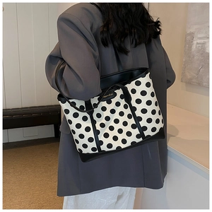 Detail of polka dot tote bag showing black leather trim and gold-tone logo plaque