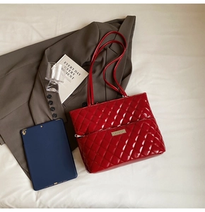 Close-up of quilted red patent leather tote bag with silver logo plaque and zipper detail
