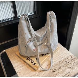 Détail du sac hobo argenté avec nœud en strass, perles et pendentif en forme de cœur