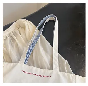 Detail of canvas tote bag showing red embroidery and blue striped webbing straps