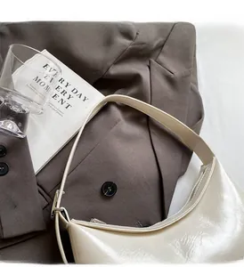 Detail of a creamy white glossy PU leather underarm bag on a dark brown blazer jacket